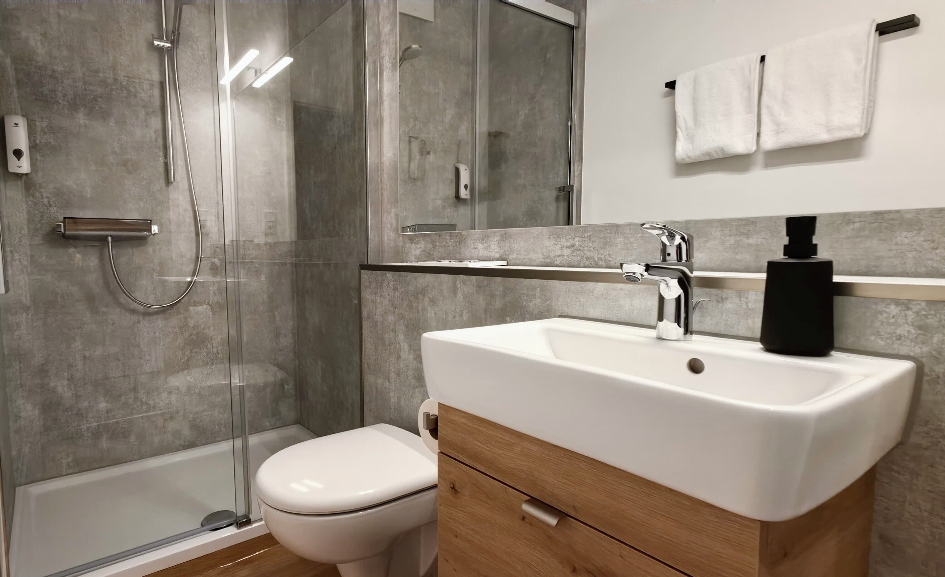 A modern bathroom with a glass shower enclosure, a white toilet, and a vanity with a sink and mirror.