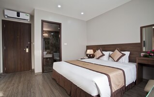 Una habitación de hotel con cama, mesita de noche, lámpara y baño a la vista a través de una puerta abierta.