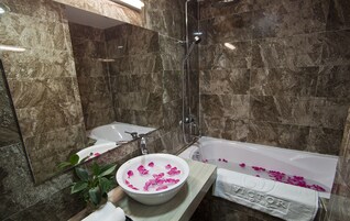 Un baño con bañera, lavabo y ducha. Hay una planta y un cuenco con pétalos de rosa en la encimera.