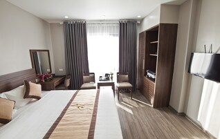 Una habitación de hotel con una cama grande, un escritorio, dos sillas, un armario y un televisor.