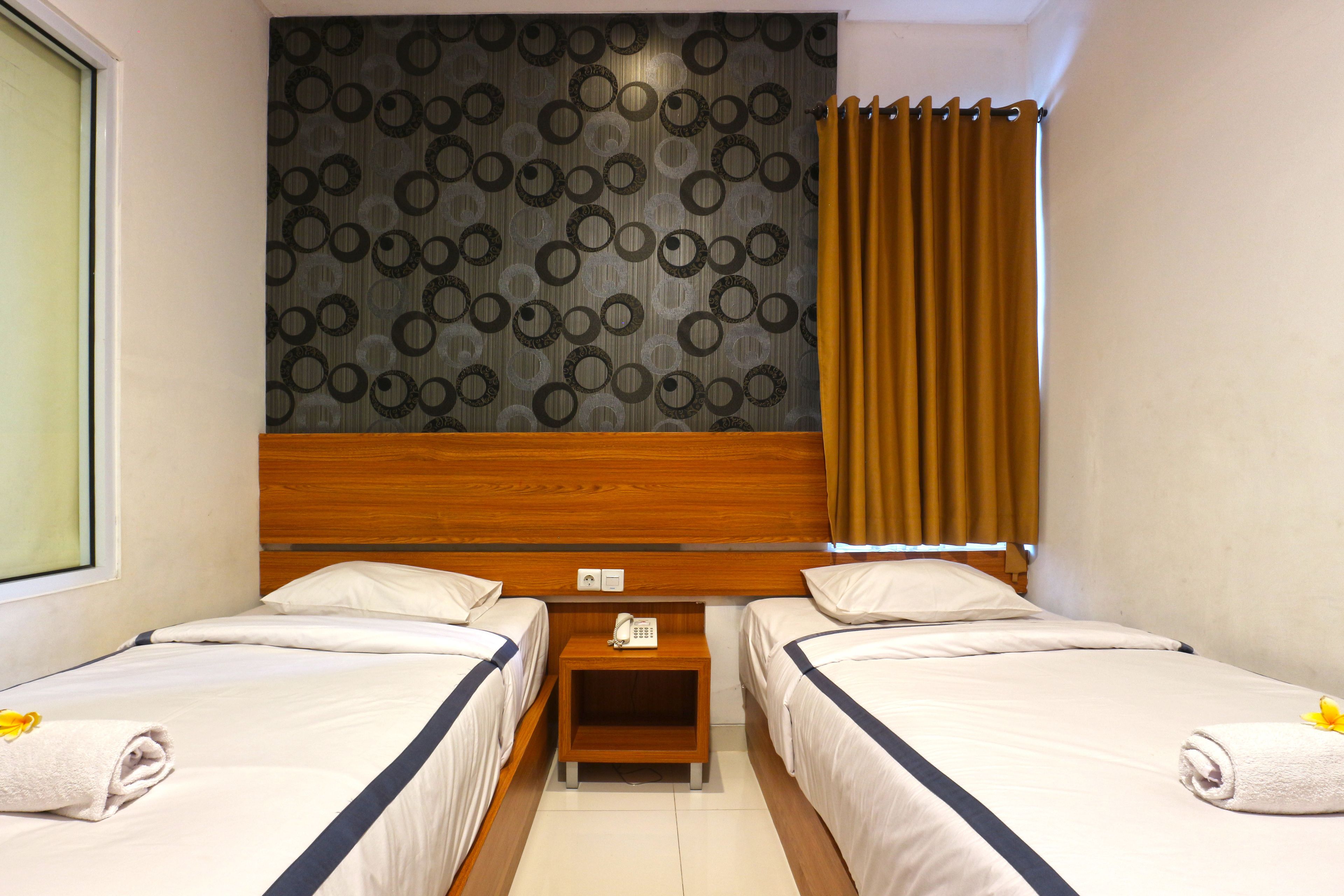 Quarto de hotel com duas camas, cabeceira de madeira, parede estampada e janela com cortinas.