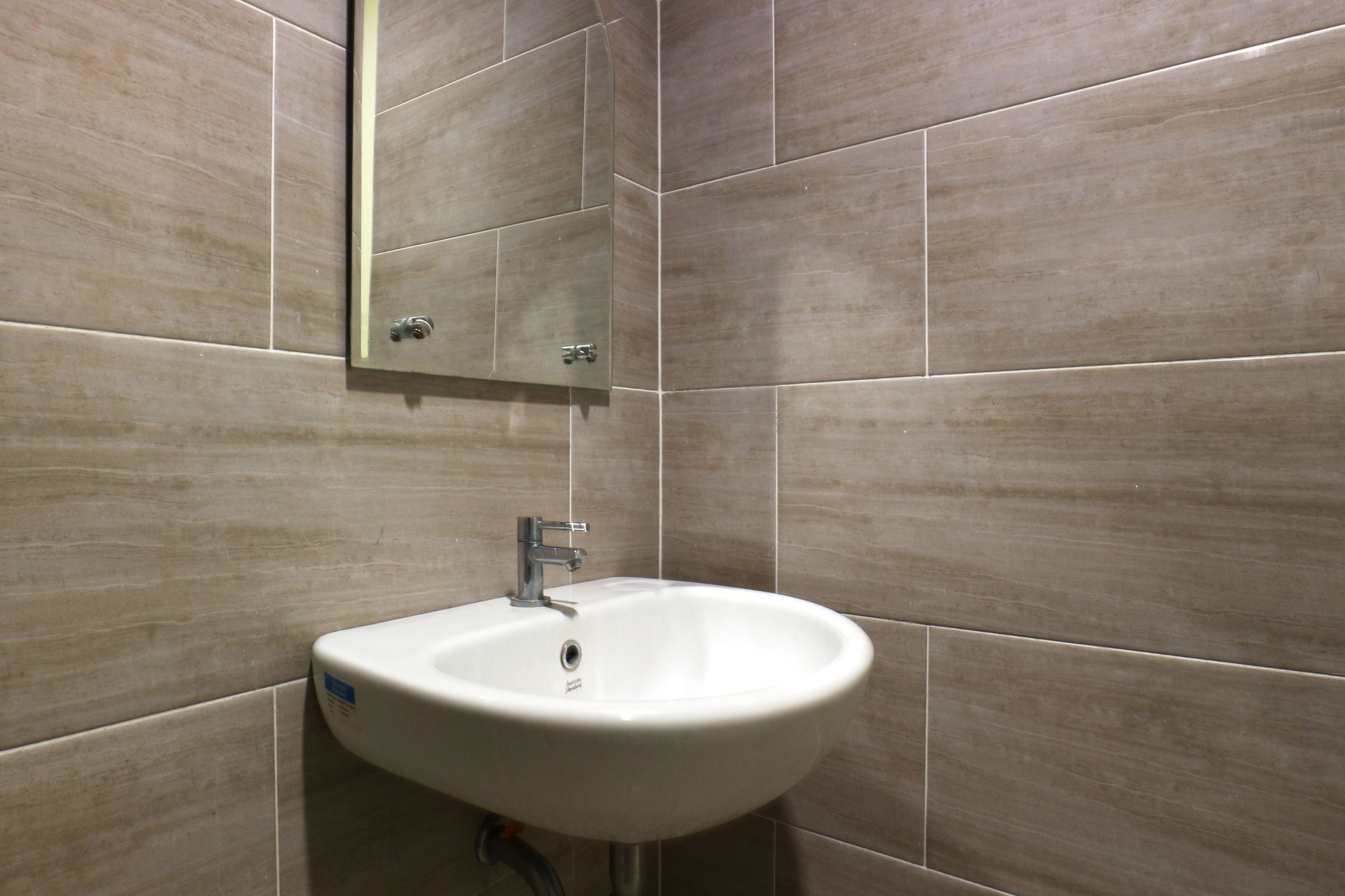Un baño con un lavamanos blanco, un espejo y baldosas color crema.