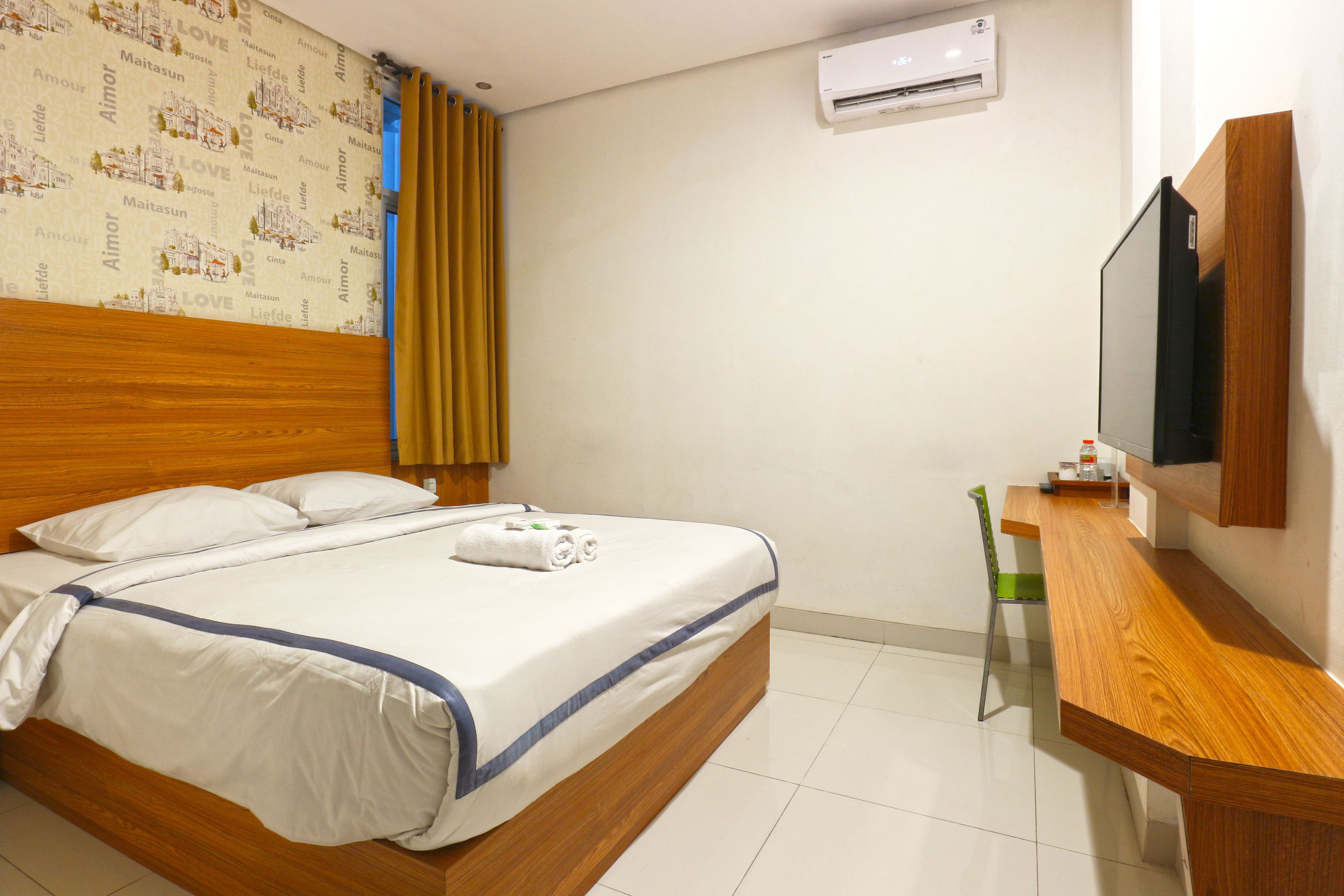 Une chambre d’hôtel avec un lit en bois, un téléviseur à écran plat, un petit bureau en bois et un climatiseur fixé au mur.