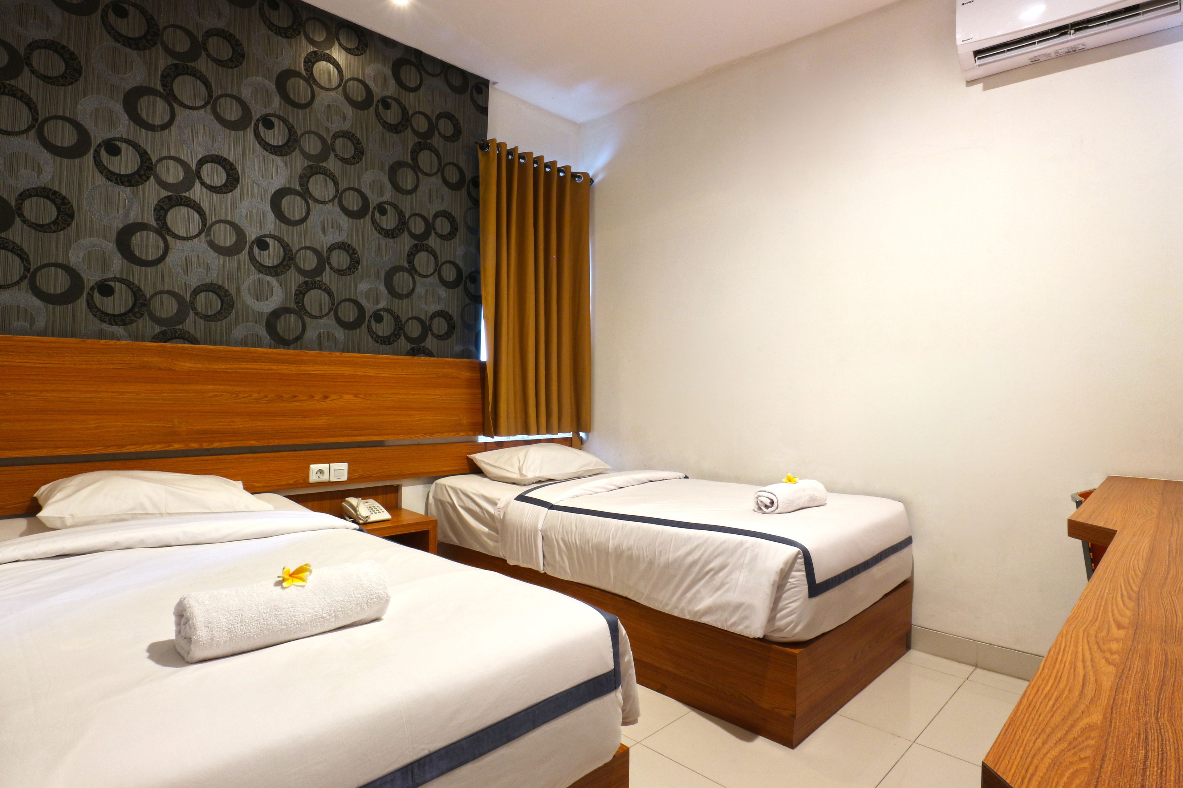 Une chambre d’hôtel avec deux lits, une tête de lit en bois, un mur à motifs et un appareil de climatisation.