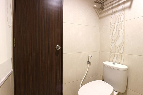 A bathroom with a wooden door, a white toilet, and beige tiled walls. - Size Inn (West Cirebon)