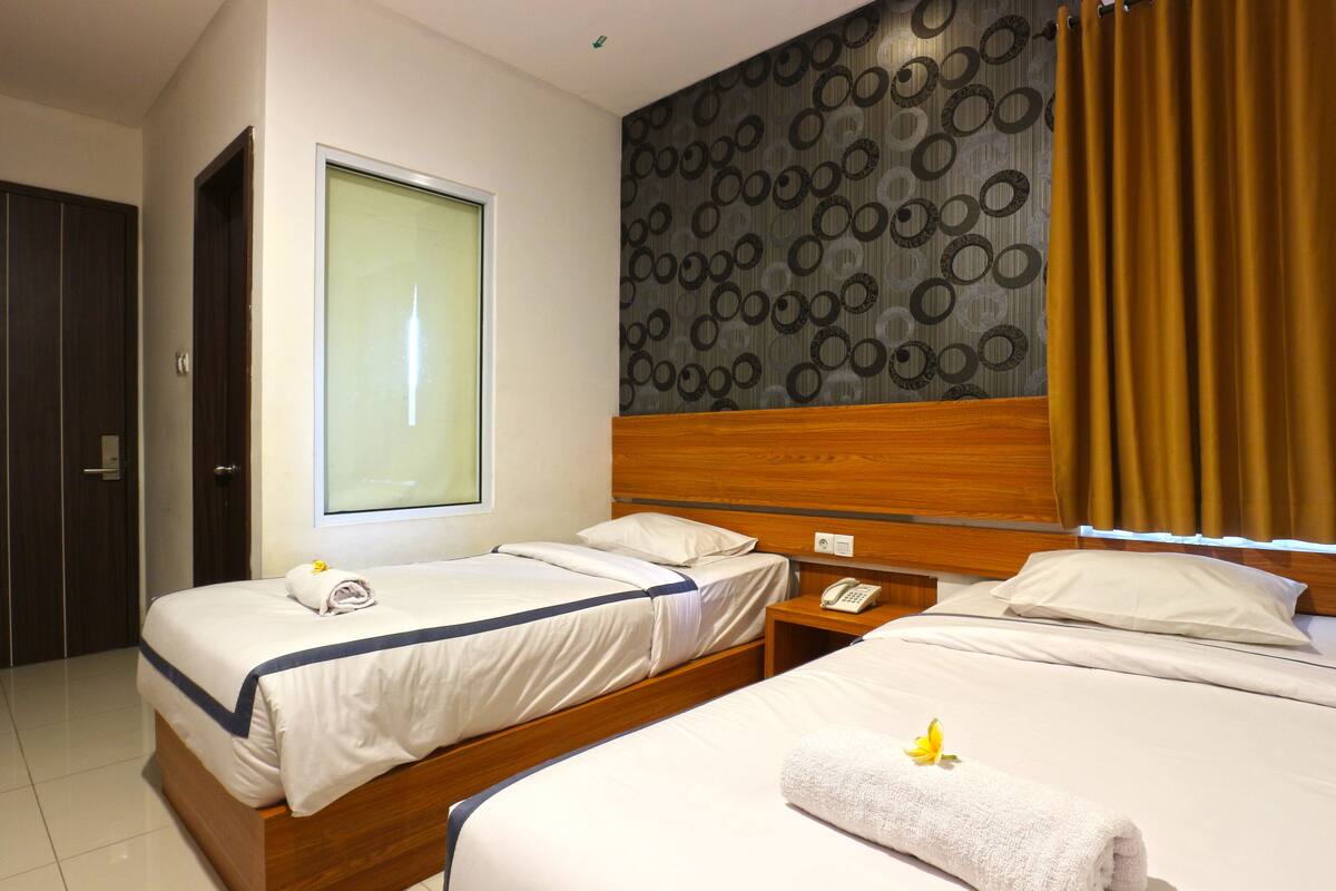 A hotel room with two beds, a wooden headboard, a large window, and a patterned wall.