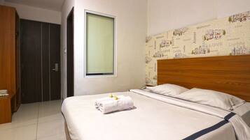 A neatly made bed with a blue accent, a wooden wardrobe, and a window with a view of a cityscape.