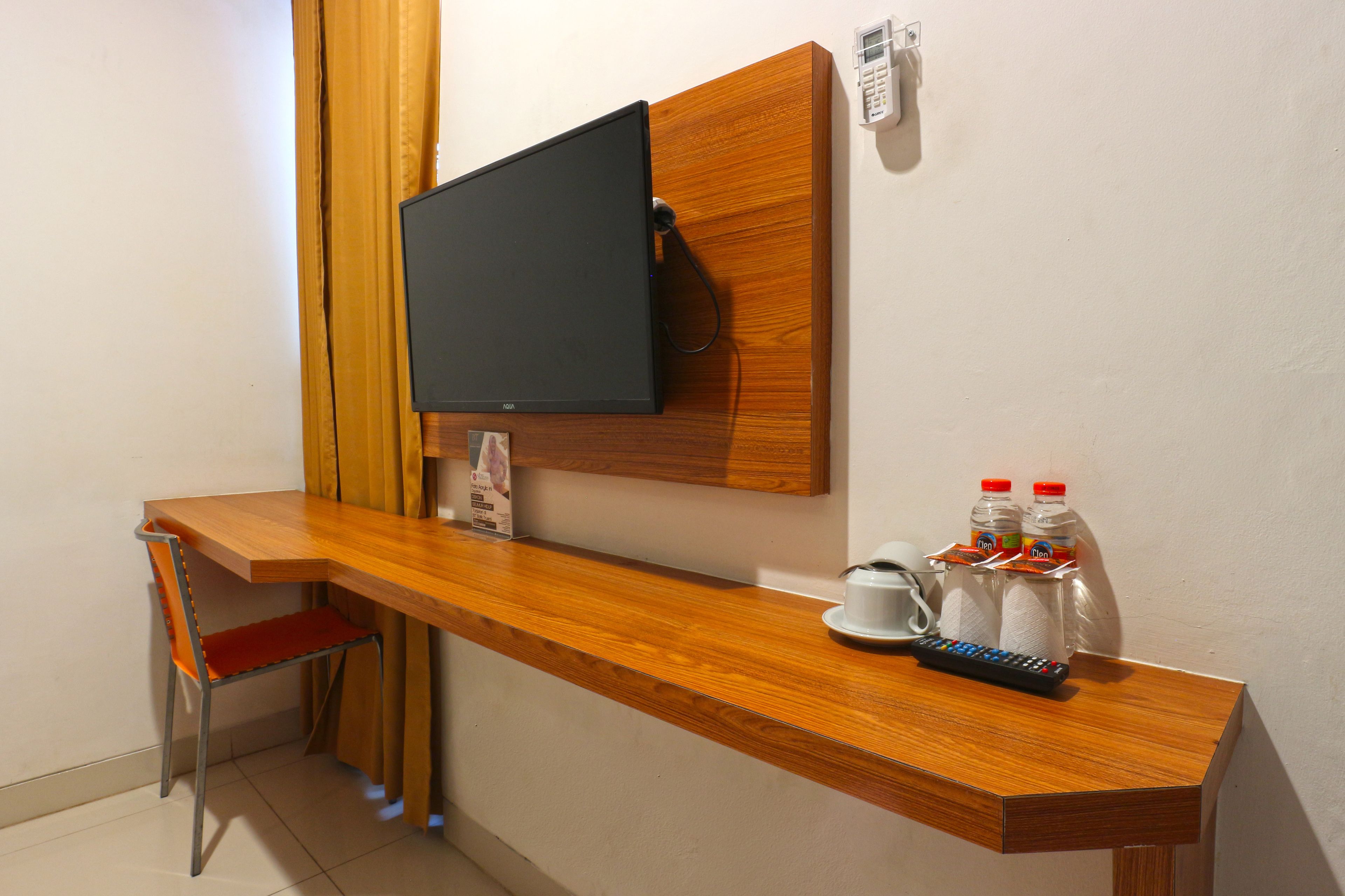 Habitación de hotel con escritorio de madera, televisor montado en la pared, una silla y una mesita con dos botellas y un control remoto.