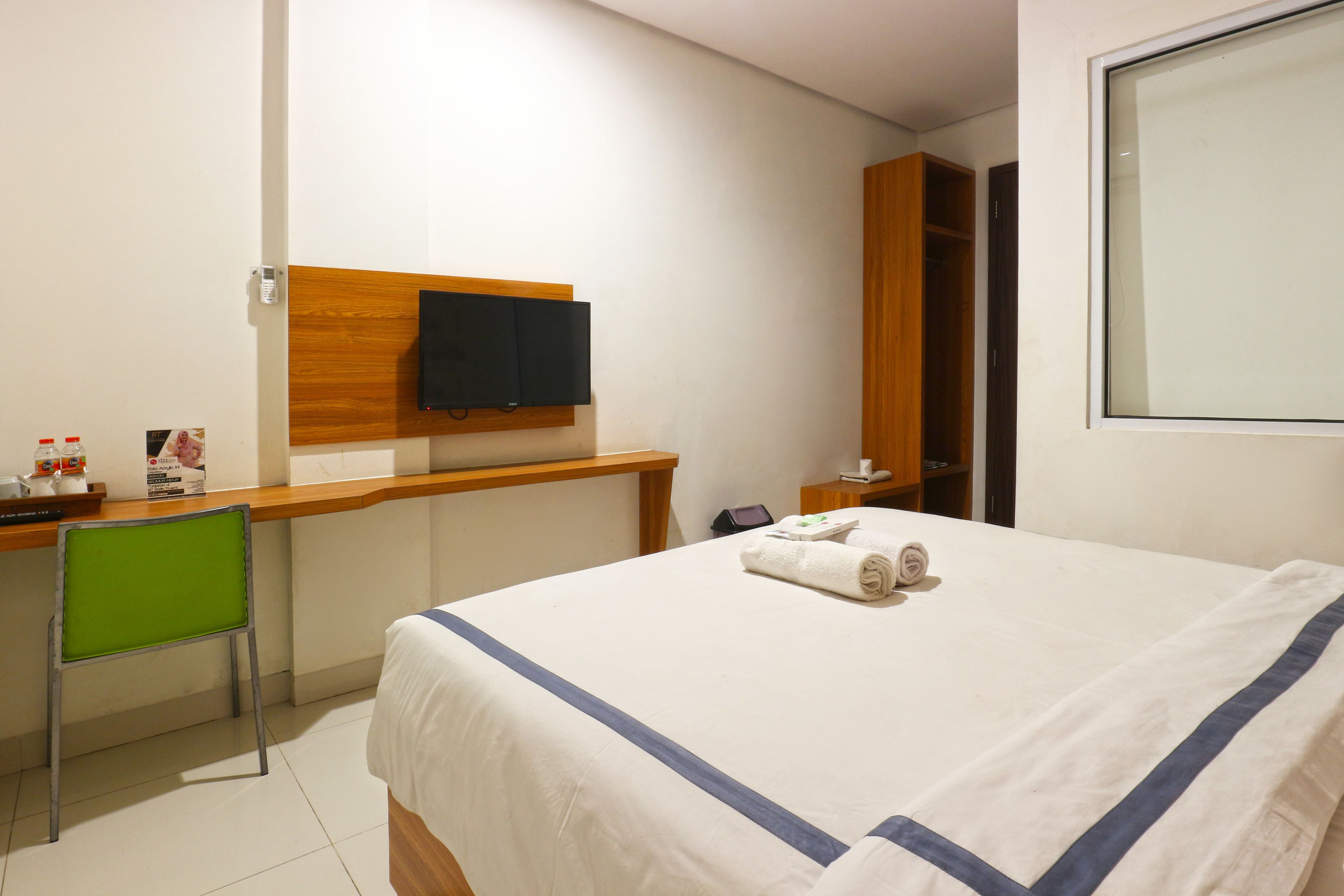 A hotel room with a bed, a desk, a chair, a television, and a wardrobe.