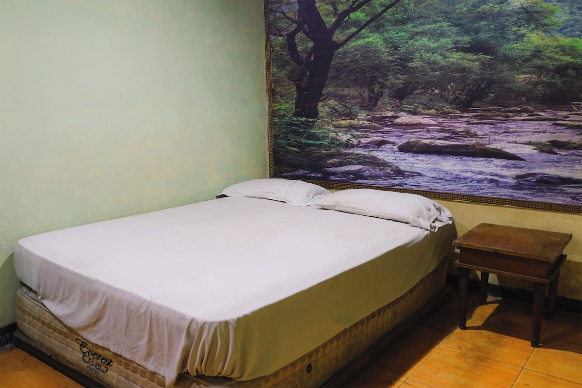 A single bed with a white mattress and pillows, a small wooden nightstand, and a wall mural of a forest stream.