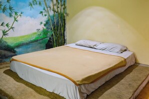 A single bed with a white and beige bedspread, a white pillow, and a wall mural of bamboo and greenery.