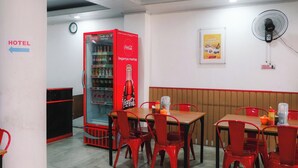 A restaurant with red chairs, tables, a Coca-Cola refrigerator, a wall clock, and a fan. - King Stone Hotel (South Tangerang)