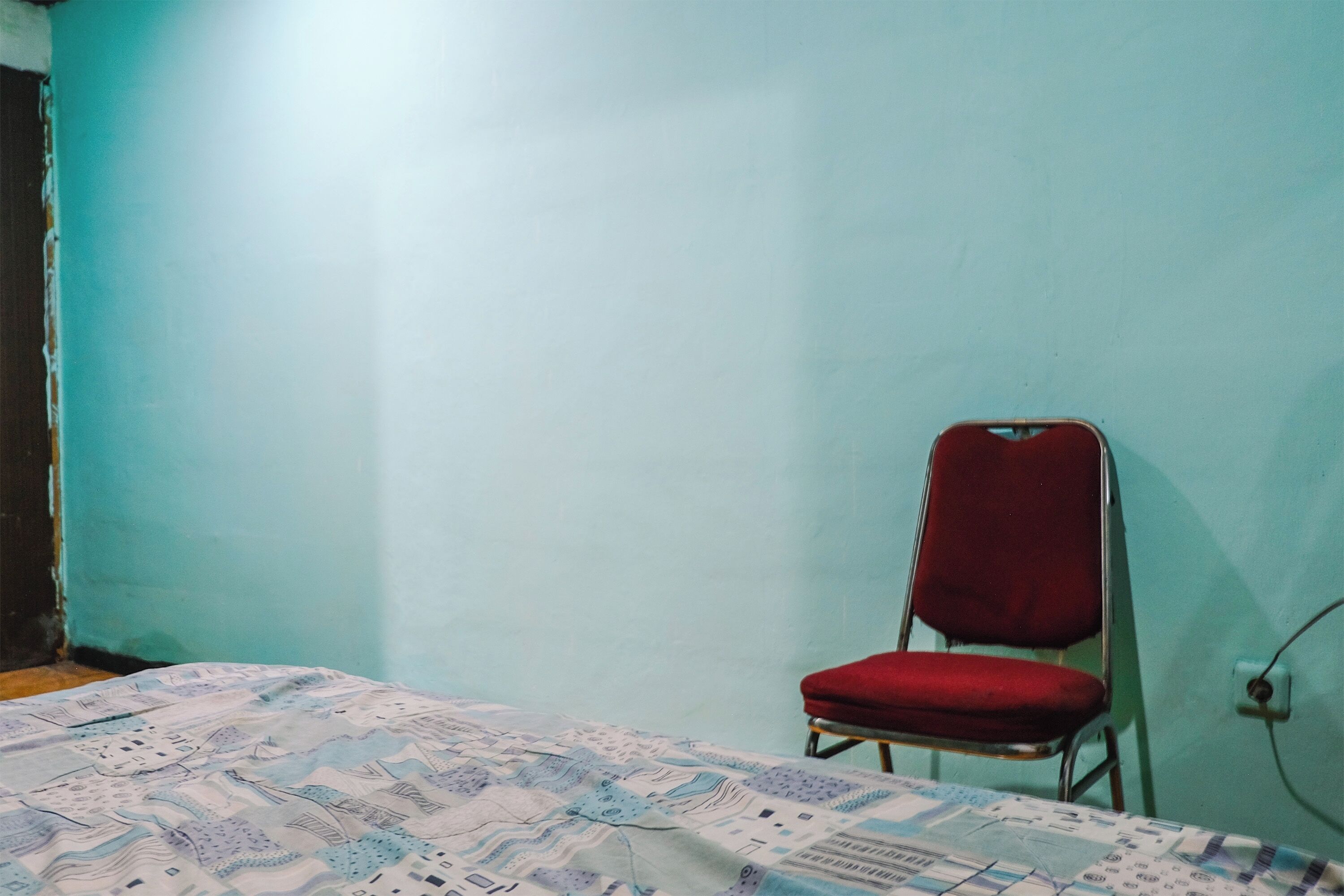 Ein Zimmer mit einem Bett, einem roten Sessel und einer schlichten Wand.