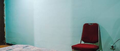A room with a bed, a red chair, and a plain wall.