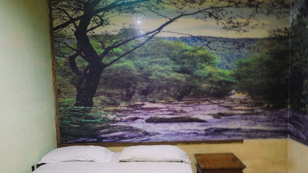 A room with a bed, a small wooden table, and a tapestry depicting a forest scene. - King Stone Hotel (South Tangerang)
