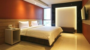 A modern hotel room with a large bed, a bedside table with a phone, and a flat-screen TV mounted on the wall. - Kampioen Bed and Breakfast (Bandung)