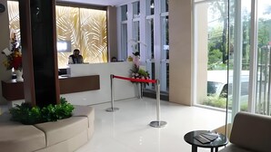 A reception area with a desk, a red barrier, and a large window offering a view of greenery. - Kampioen Bed and Breakfast (Bandung)