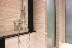 A modern bathroom with a shower, a black countertop, and light wood-patterned walls. - Kampioen Bed and Breakfast (Bandung)