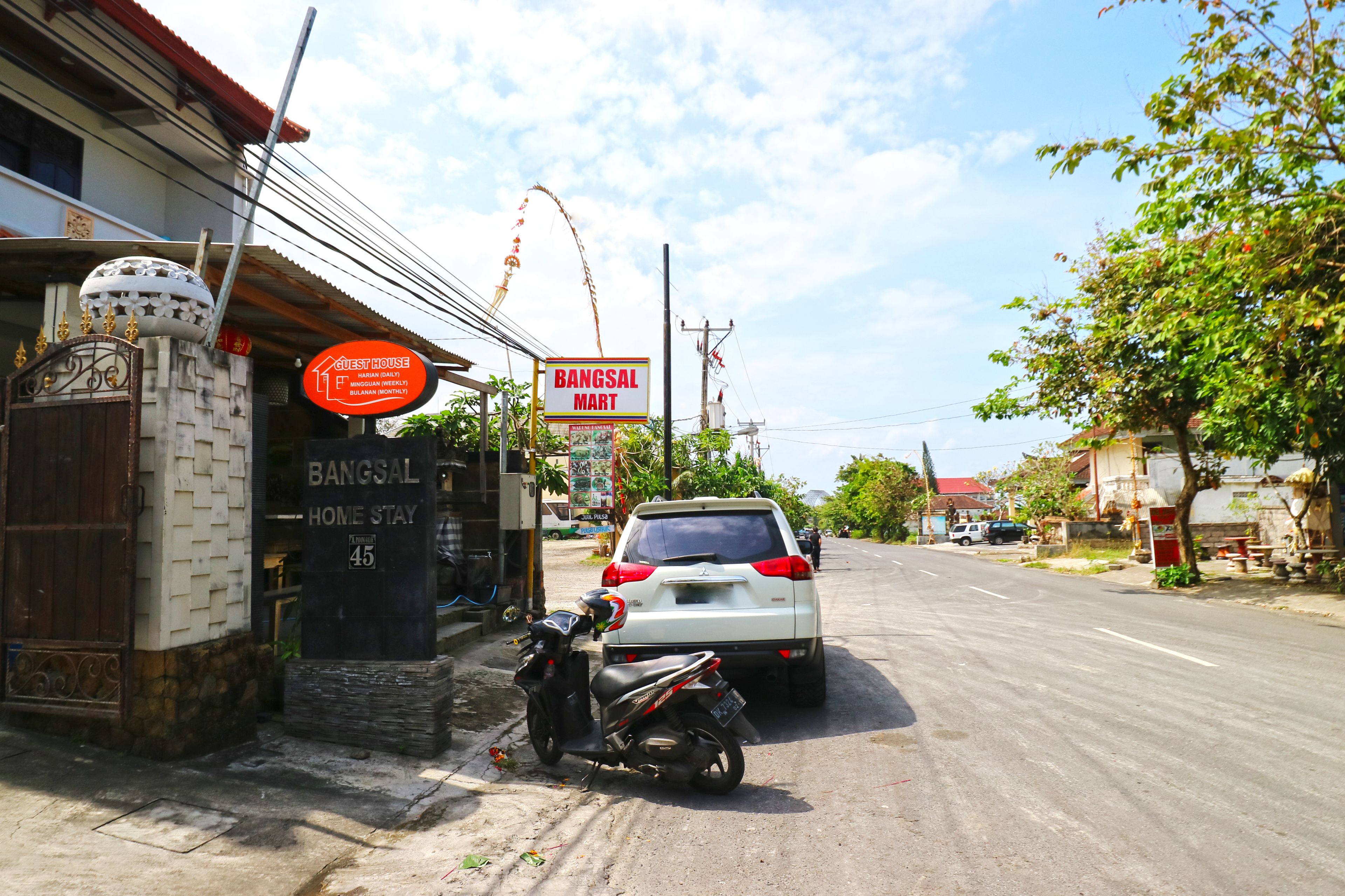 A street view with a white car parked on the side, a motorcycle, and a building with a sign for 'BANGSAL MART'.