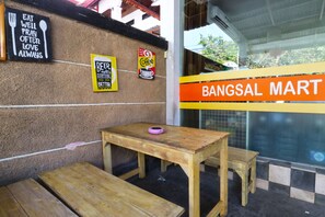 A wooden table and benches outside a building with signs on the wall, including one for a mart. - Bangsal Homestay (Denpasar)