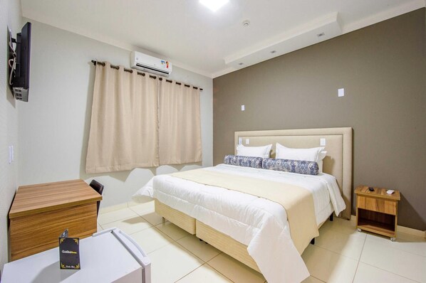 A hotel room with a bed, a wooden desk, a small bedside table, and a wall-mounted TV.
