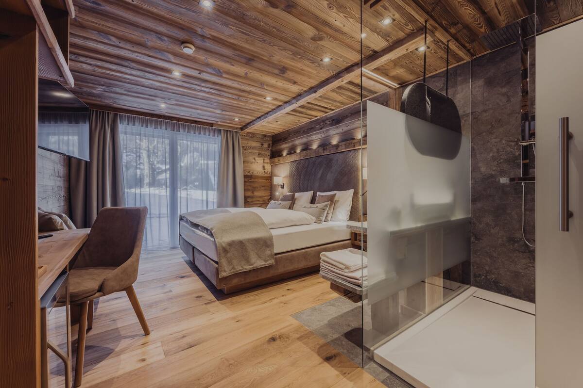 Un dormitorio moderno con techo de madera, cabina de ducha de vidrio y una cama grande con cabecera.