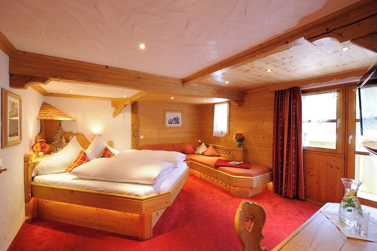 Una habitación de cabaña de madera con una cama grande, un sofá más pequeño y una ventana con cortinas.