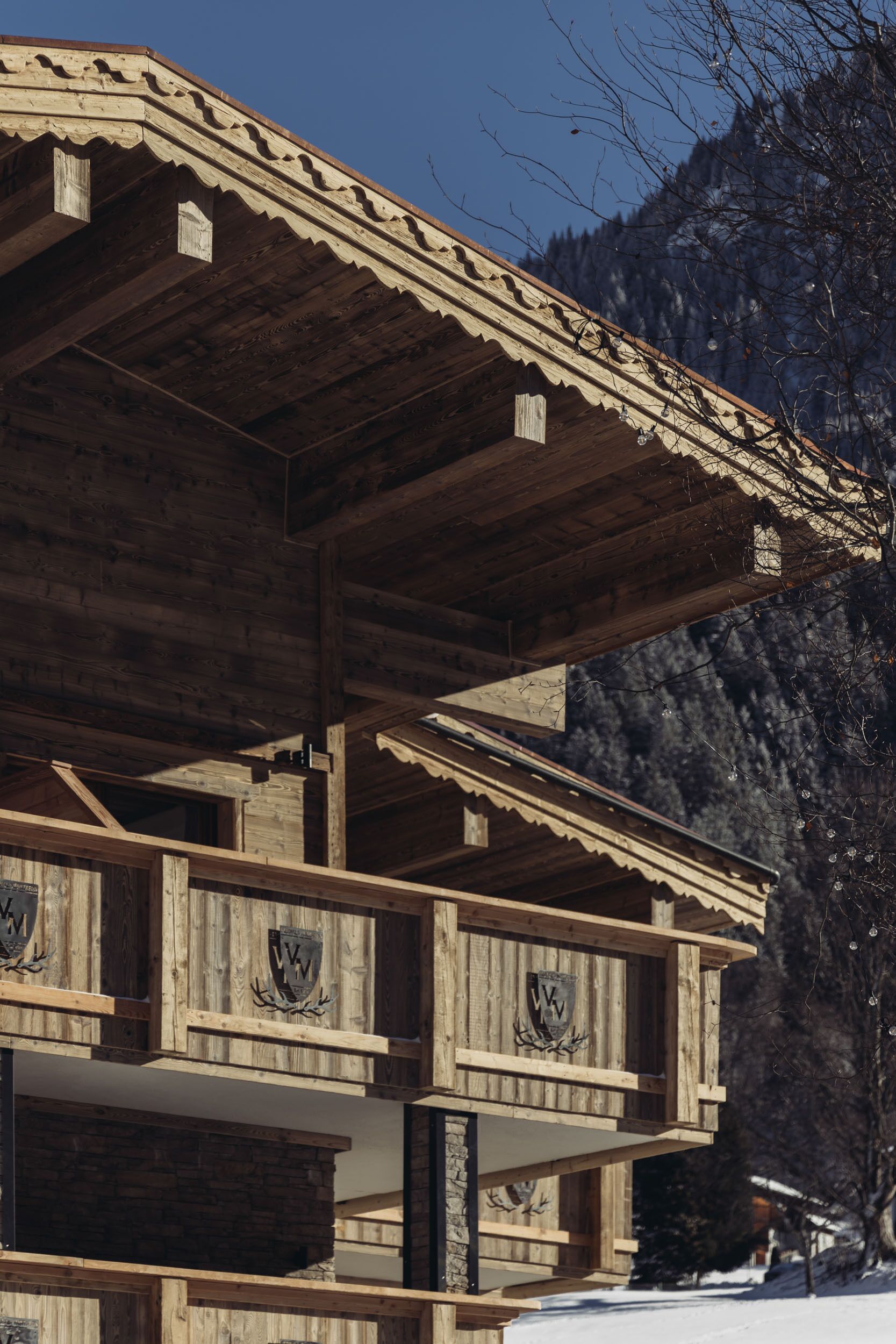 Een houten chalet met een schuin dak en meerdere balkons, met een besneeuwd berglandschap op de achtergrond.