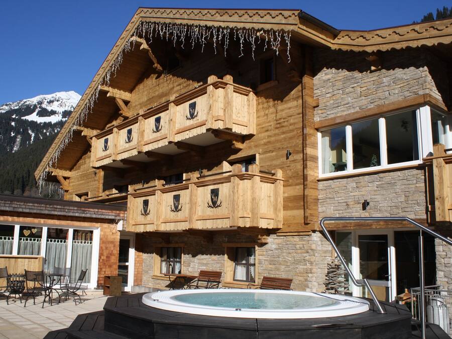 A wooden chalet with a balcony, a hot tub, and a mountain view.