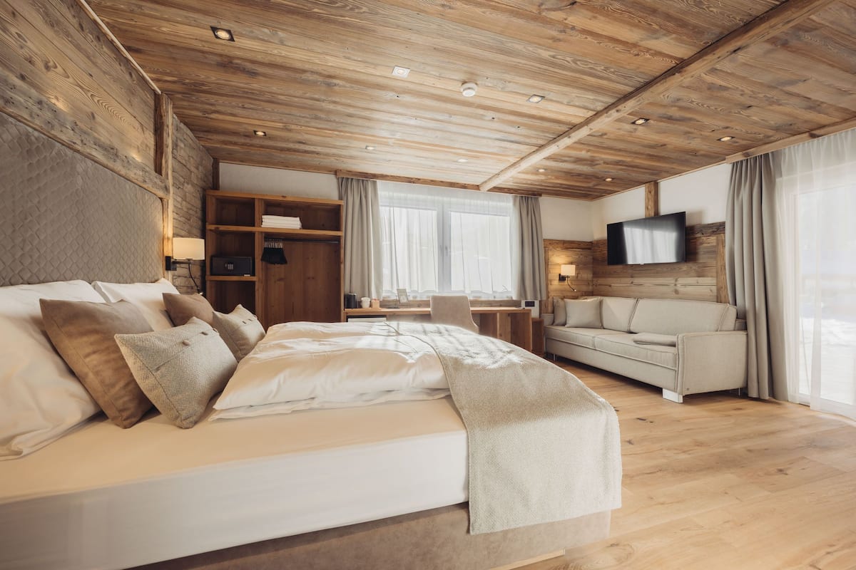 Una habitación de hotel moderna con techo de madera, una cama grande, un sofá, un escritorio y un televisor montado en la pared.