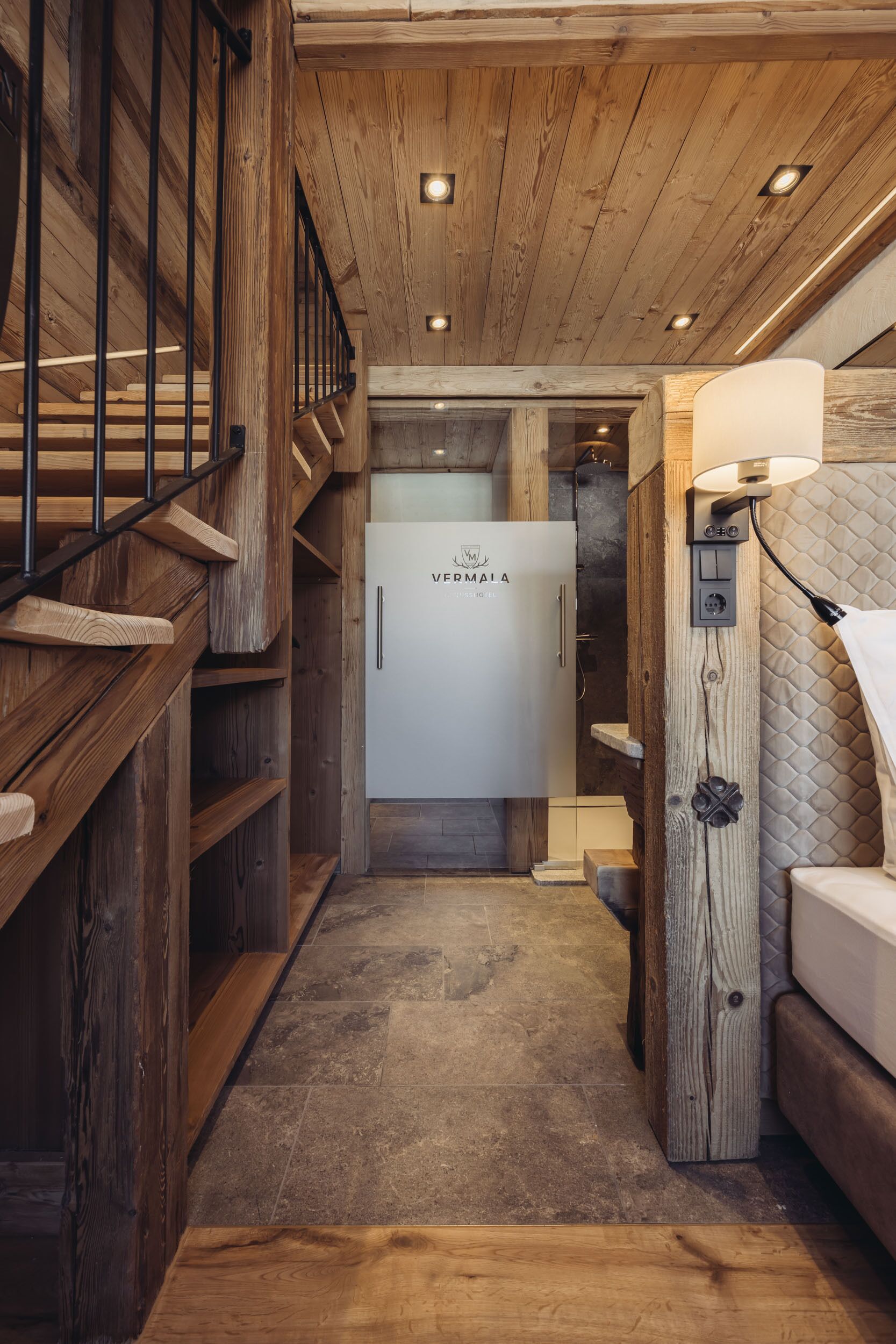 Un couloir étroit aux murs en bois et un escalier. On peut voir un réfrigérateur blanc portant la marque « VERMAIA ».
