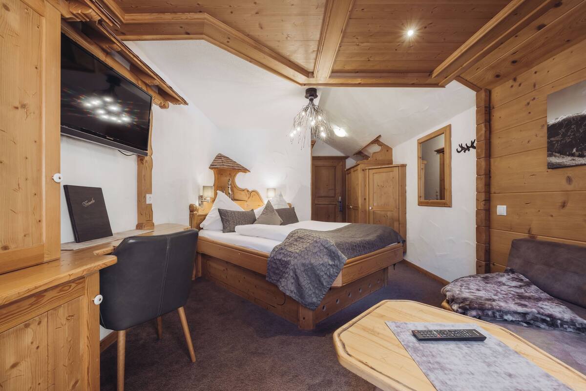 Un dormitorio con piso de madera, una cama, un escritorio, un televisor y una lámpara en el techo.