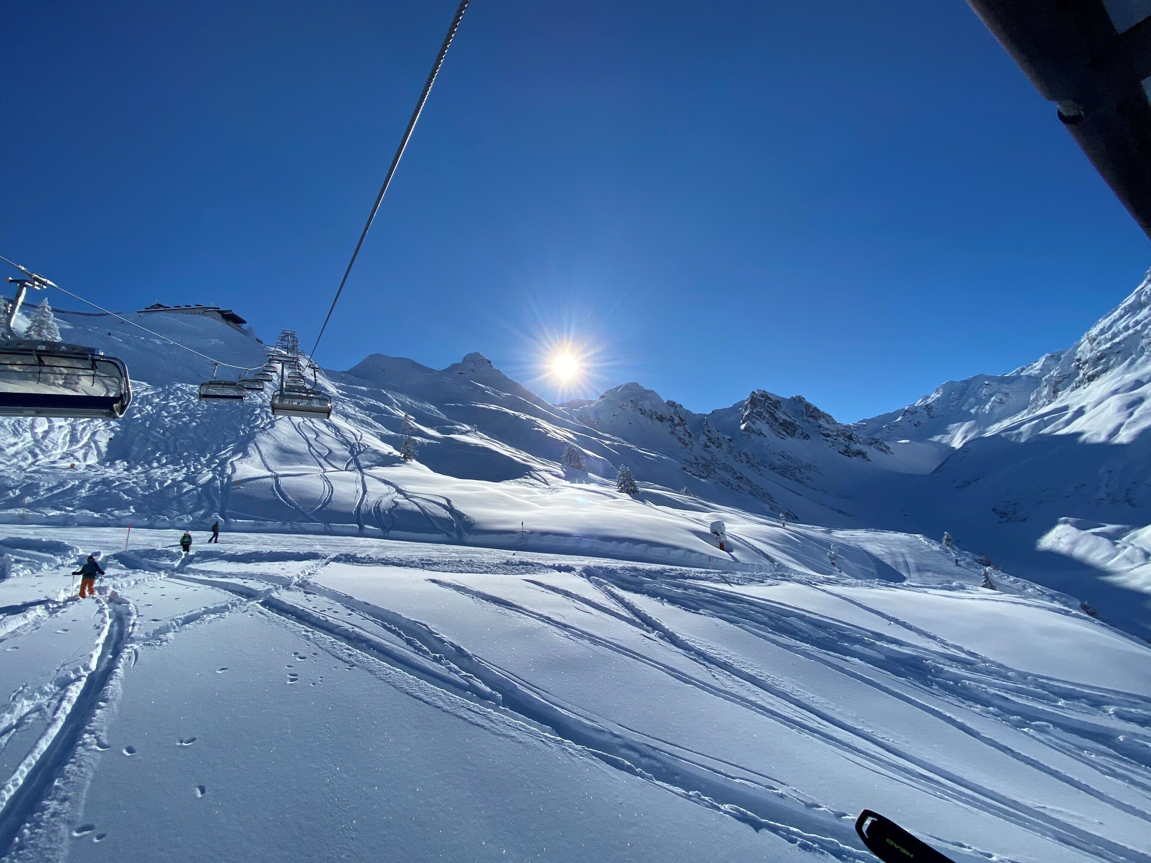 Eine Skipiste mit blauem Himmel und Sonnenschein, mit Sesselliften und Abfahrten.