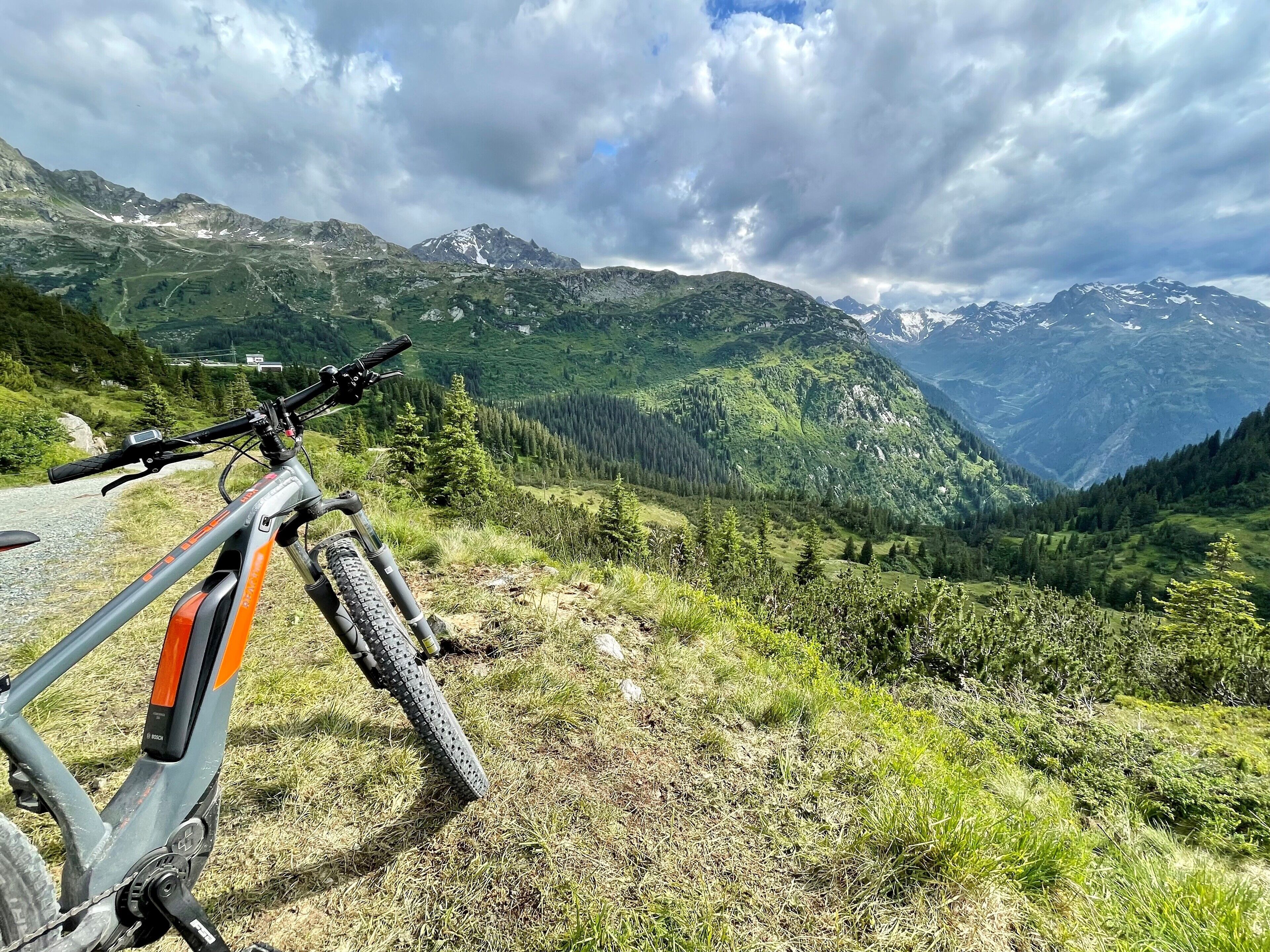 A mountain bike parked on a grassy path with a view of a valley and mountains in the background.