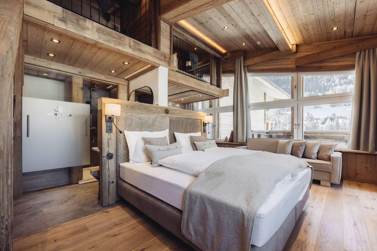 Un dormitorio amplio con una cama grande, techo de madera y vistas al paisaje nevado a través de la ventana.