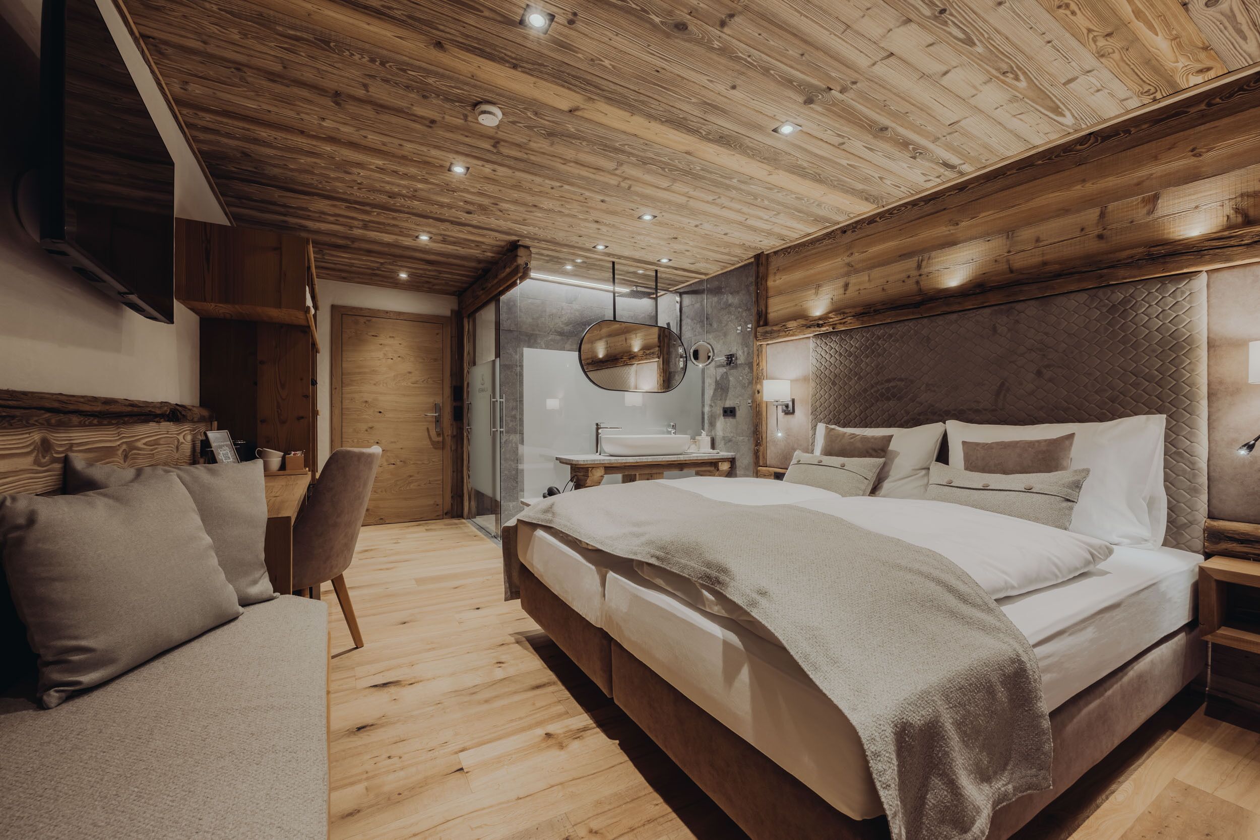 Un dormitorio con techo de madera, una cama grande, una mesita de noche, una silla y un espejo.