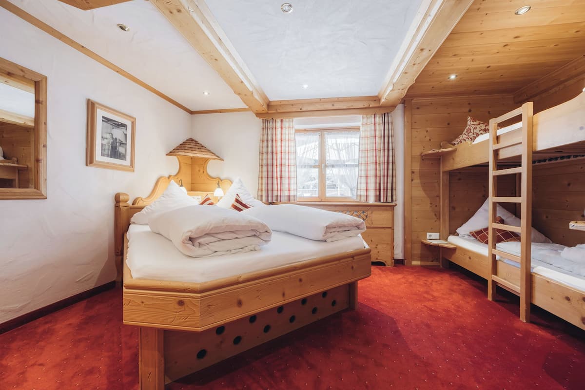 Habitación con literas de madera, una cama individual y una litera, cabecera de madera, una mesita pequeña y una ventana con cortinas de cuadros.