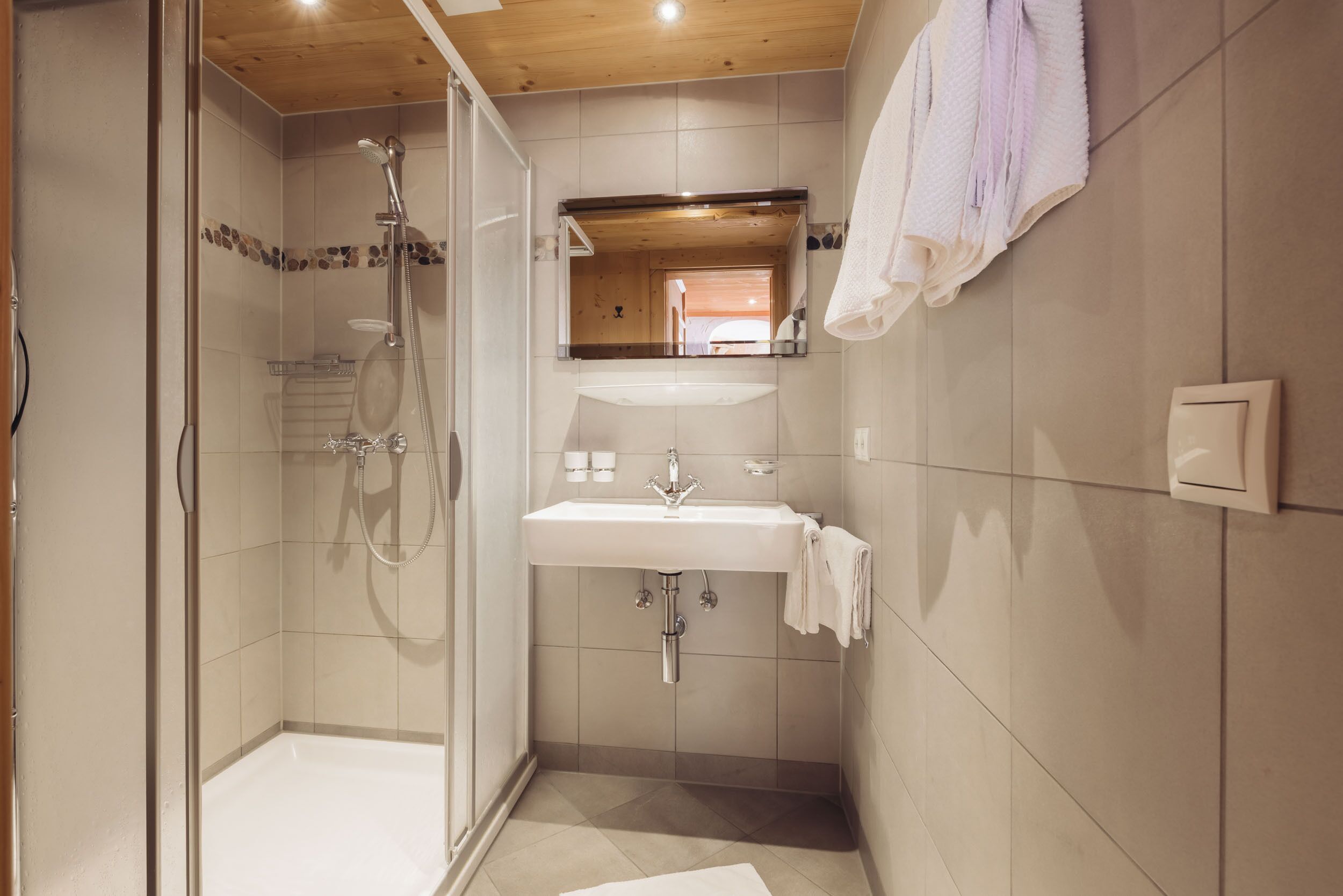Een moderne badkamer met een douchecabine, een wastafel met spiegel erboven en een handdoek aan de muur.