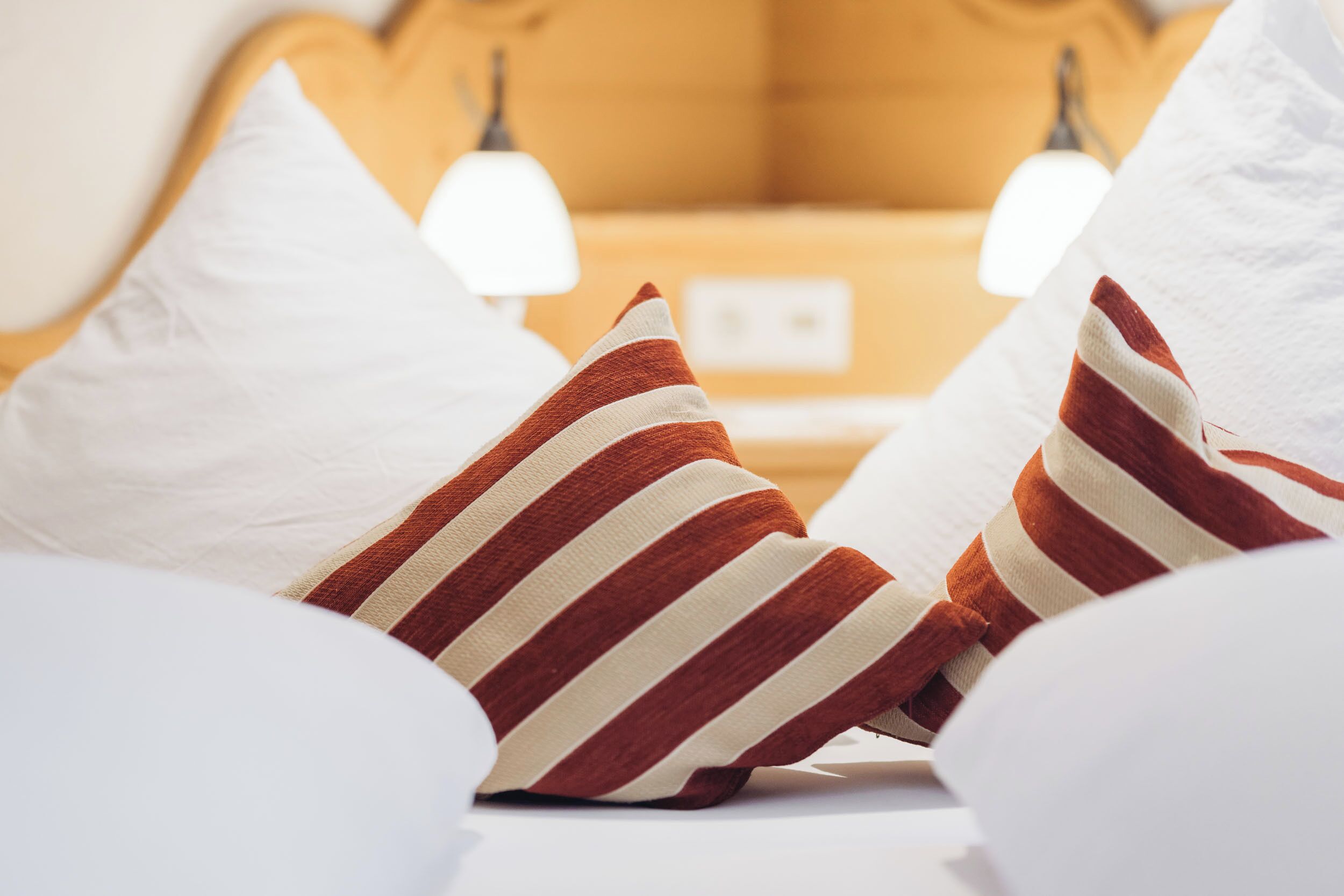 A bed with white and striped pillows, a mustard-colored headboard, and two bedside lamps.