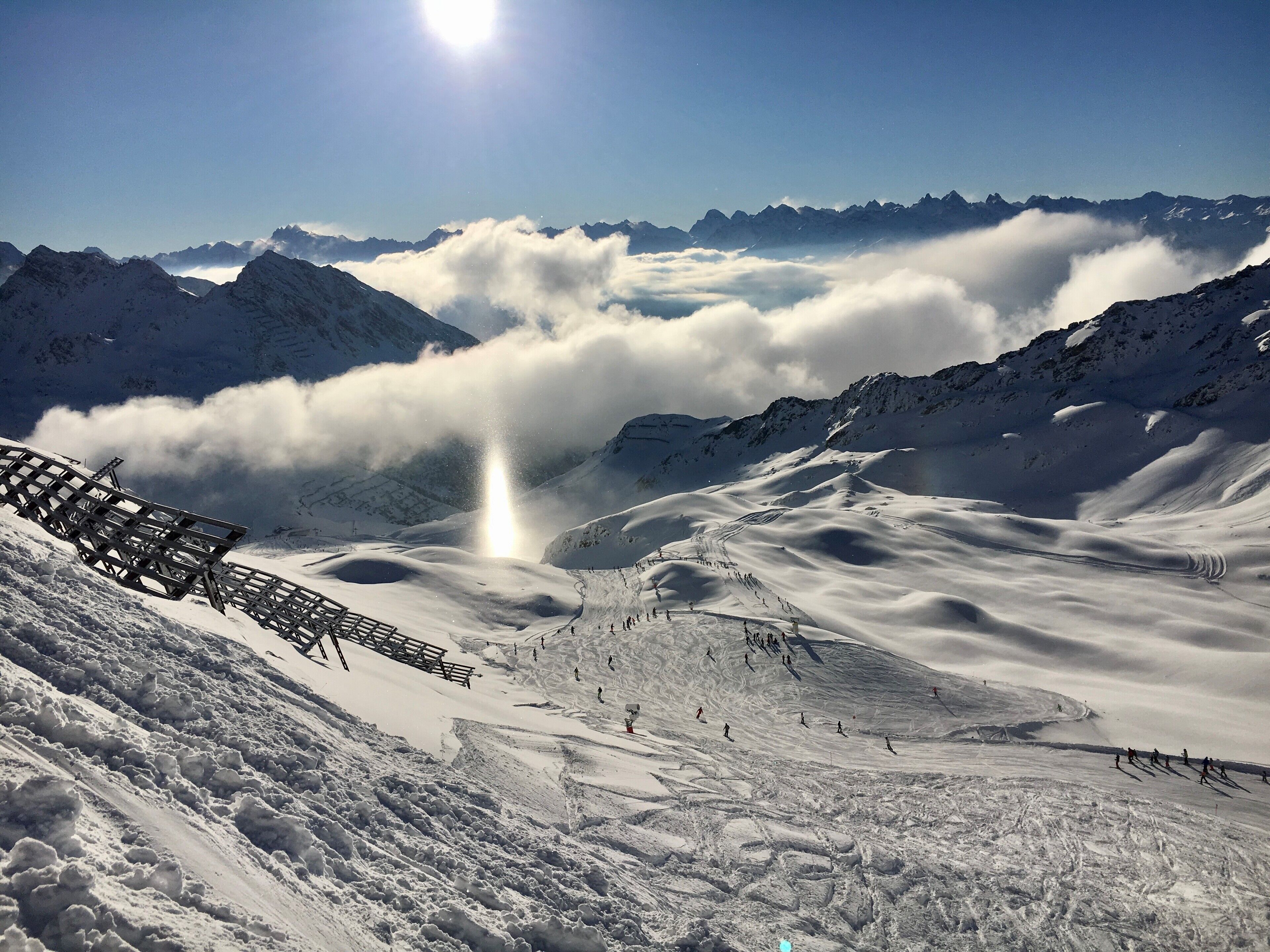 Eine verschneite Berglandschaft mit einer Skipiste, einem Holzzaun und blauem Himmel.