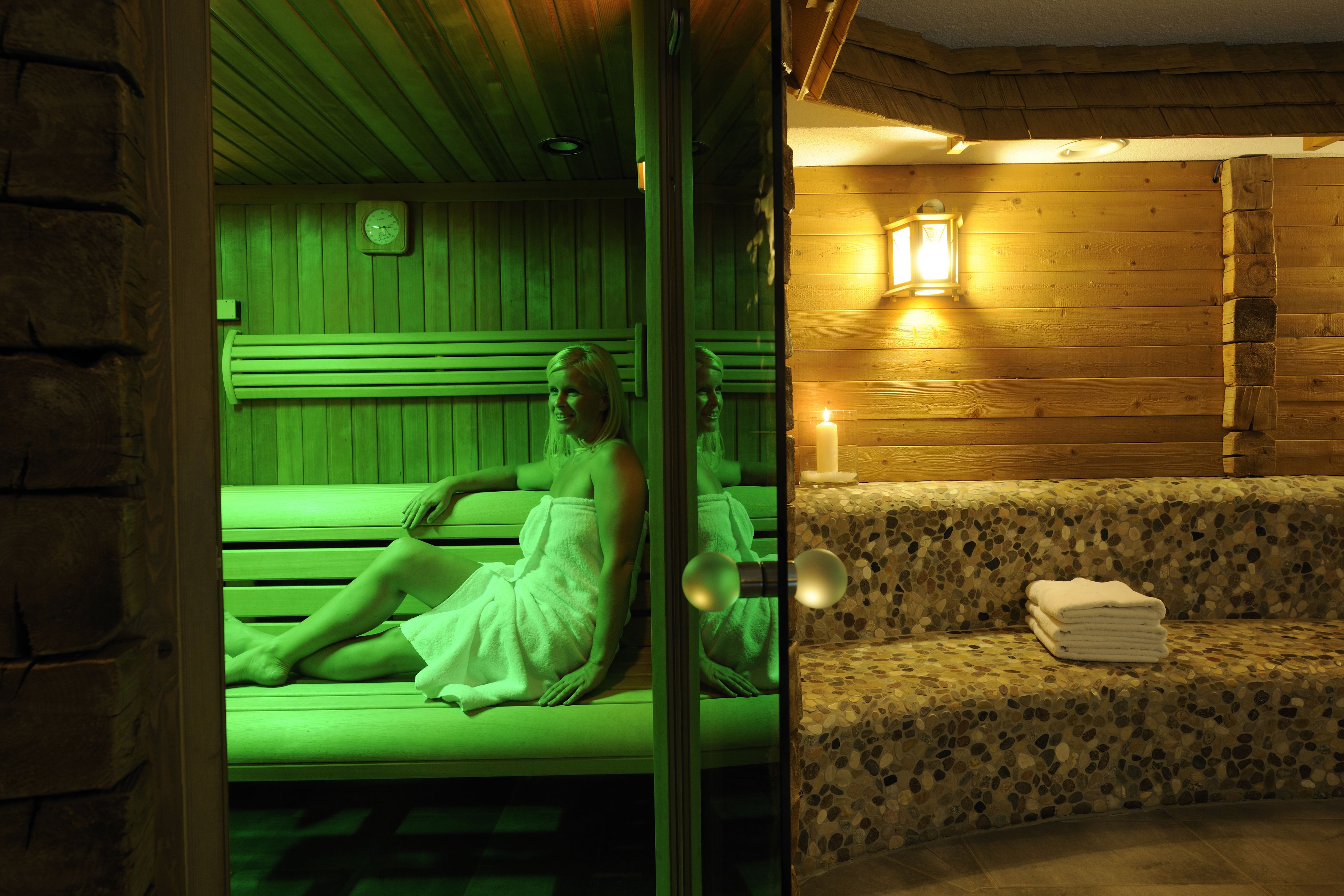 A sauna room with a wooden bench, a bench with a towel, and a wall-mounted clock.