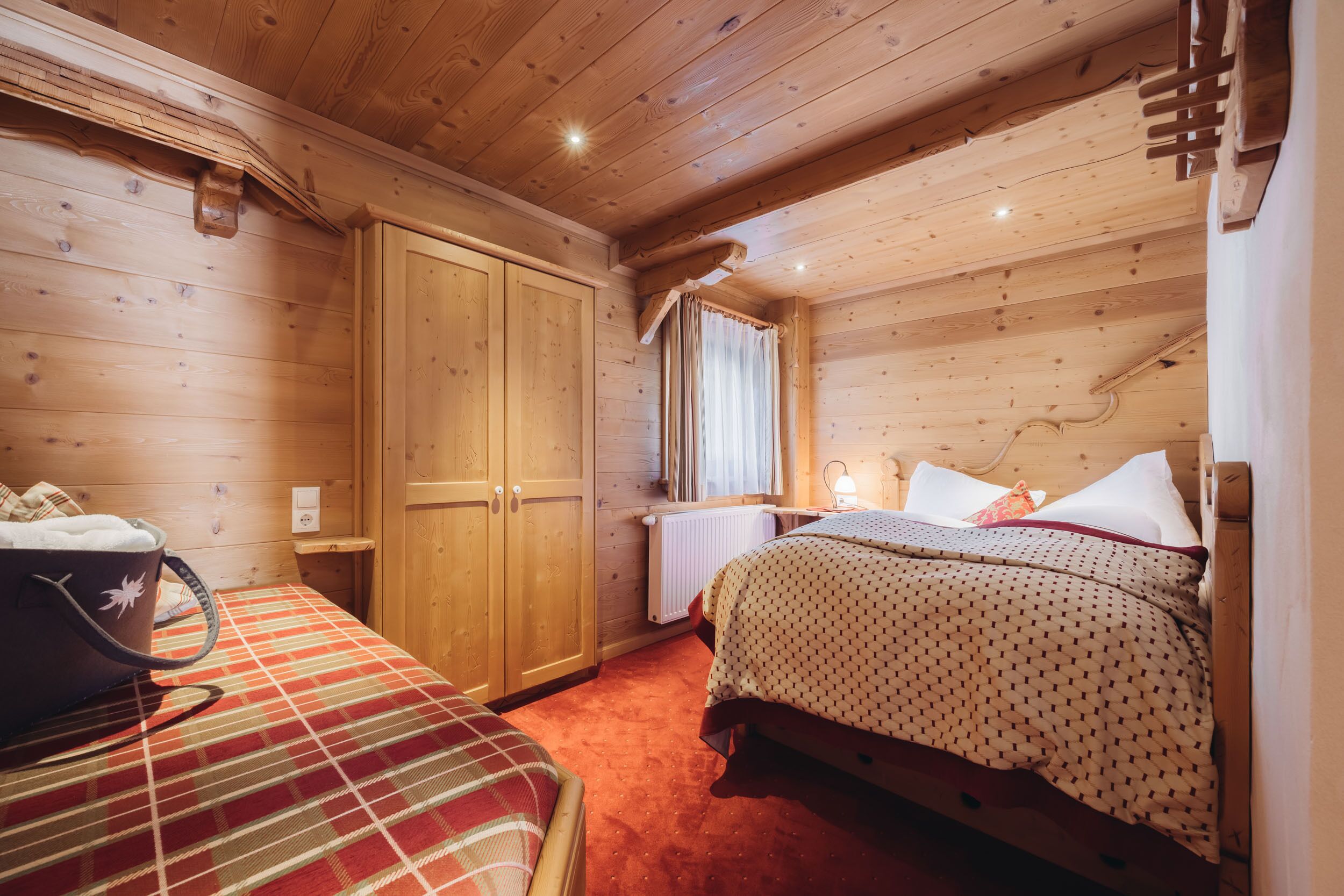 Un dormitorio de cabaña de madera con una cama, un armario y una maleta sobre una colcha a cuadros.
