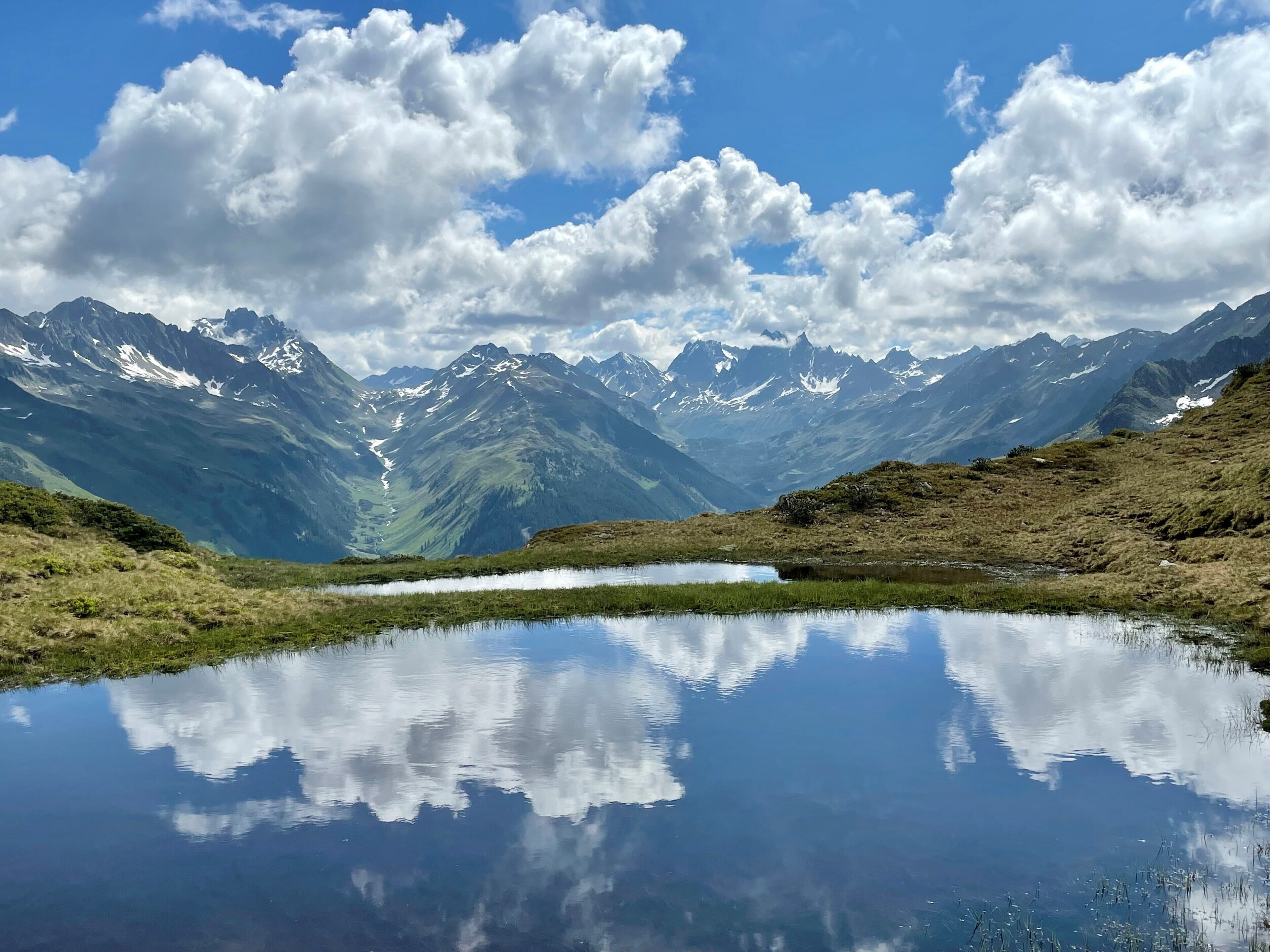 A mountain landscape with a clear lake reflecting the sky and clouds.