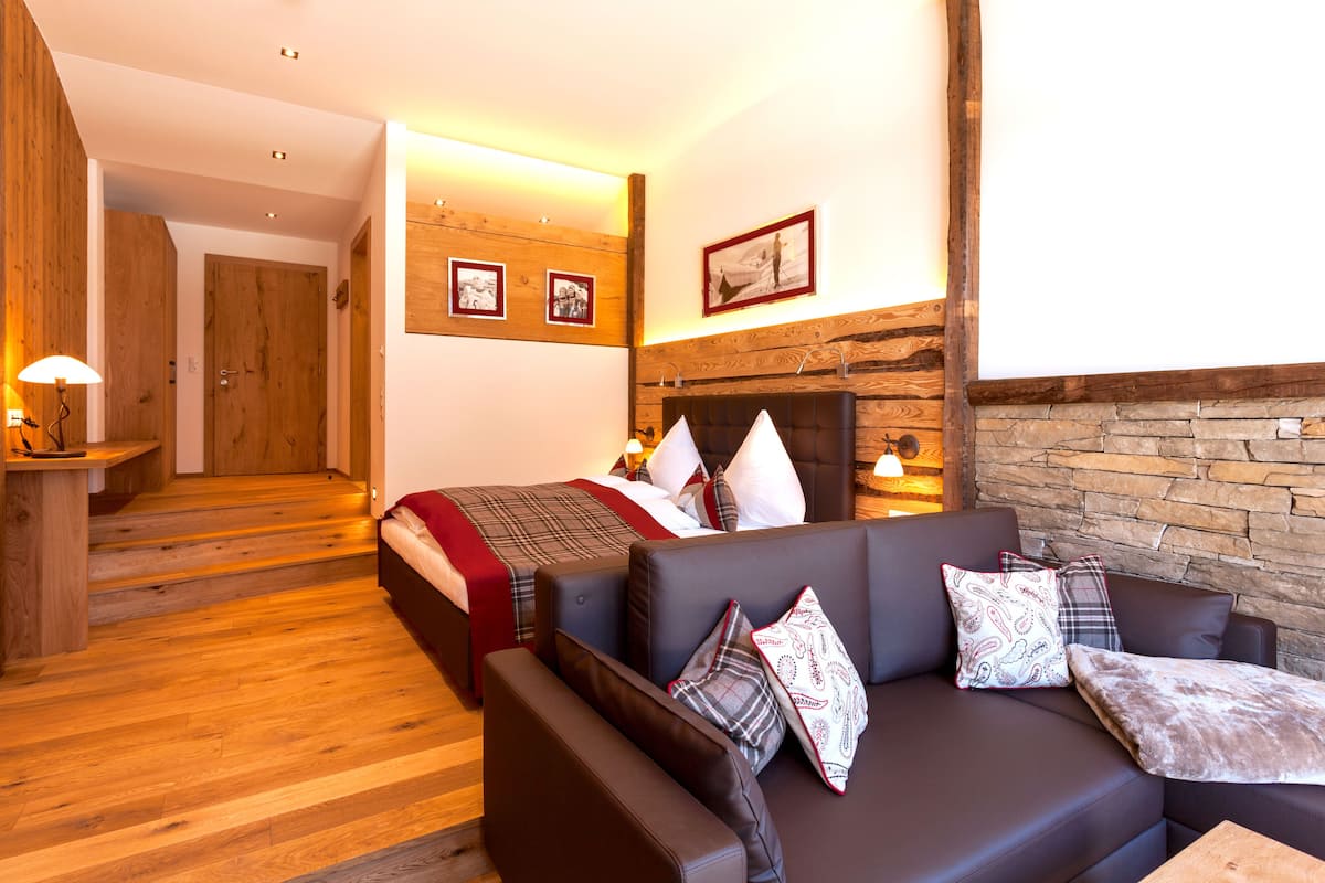 Una habitación de hotel con piso de madera, una cama con manta roja, un sofá con cojines estampados y una chimenea de piedra.