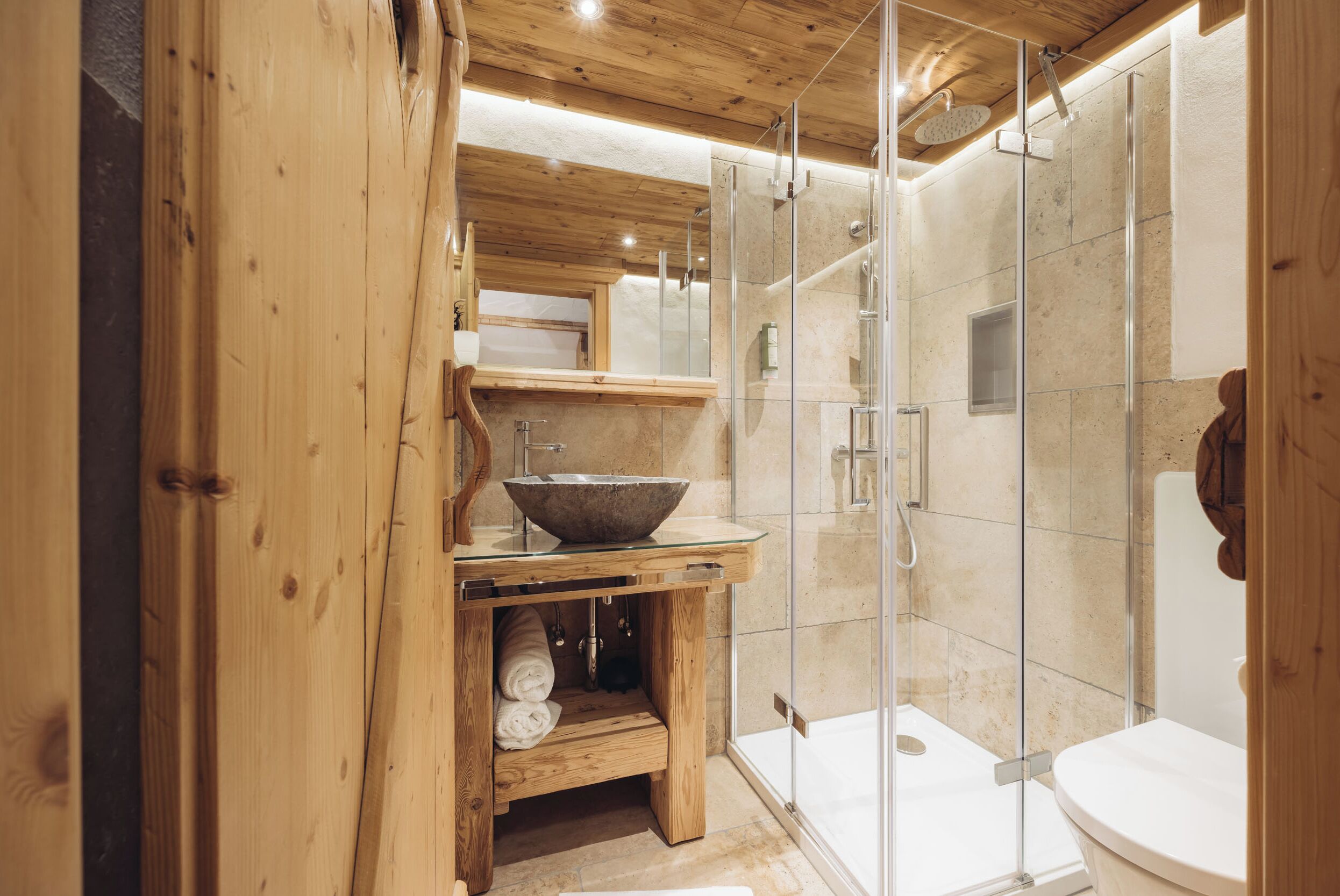 Un baño moderno con un mueble de tocador de madera, cabina de ducha de vidrio y un inodoro blanco.