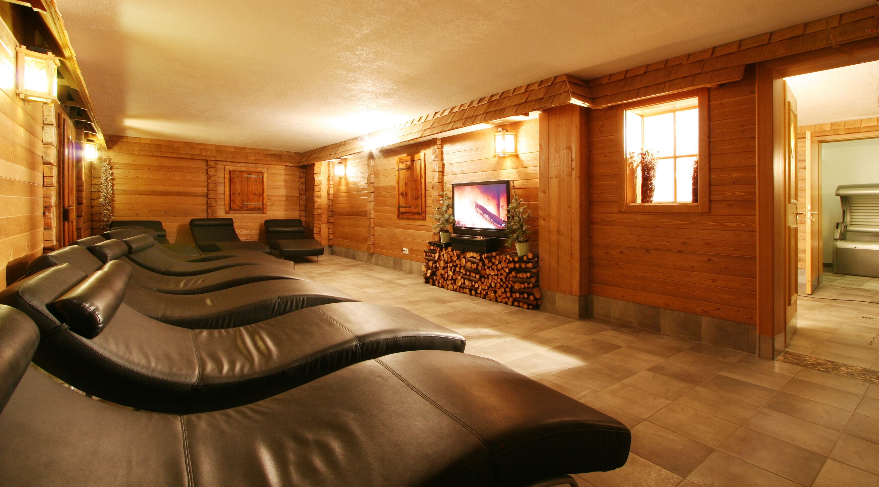 Sala de sauna con varias sillas de masaje, un televisor y una pared de troncos.