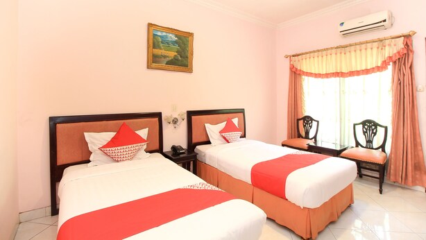 A hotel room with two beds, a painting on the wall, an air conditioner, and a window with curtains. - Kartika Homestay Syariah (Surabaya)