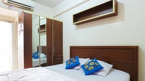 Une chambre à coucher avec une tête de lit en bois, un lit avec une literie blanche et des coussins à motifs floraux bleus, une armoire et une petite étagère en bois au-dessus du lit.