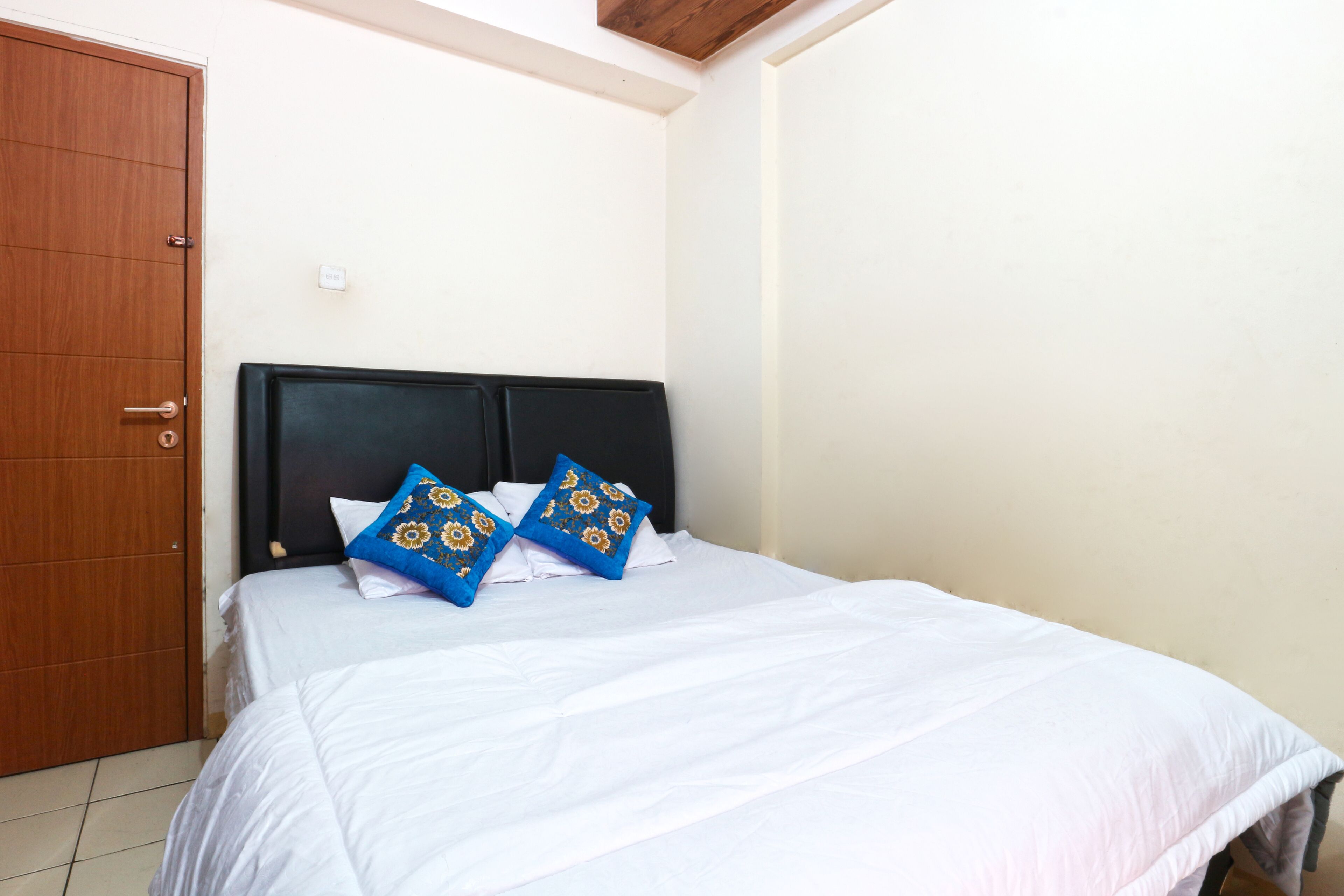 A bedroom with a wooden door, a black headboard, and a white bedspread.