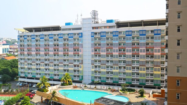 Un hôtel à plusieurs étages doté d’une piscine centrale, de balcons à chaque étage et d’un espace de stationnement.